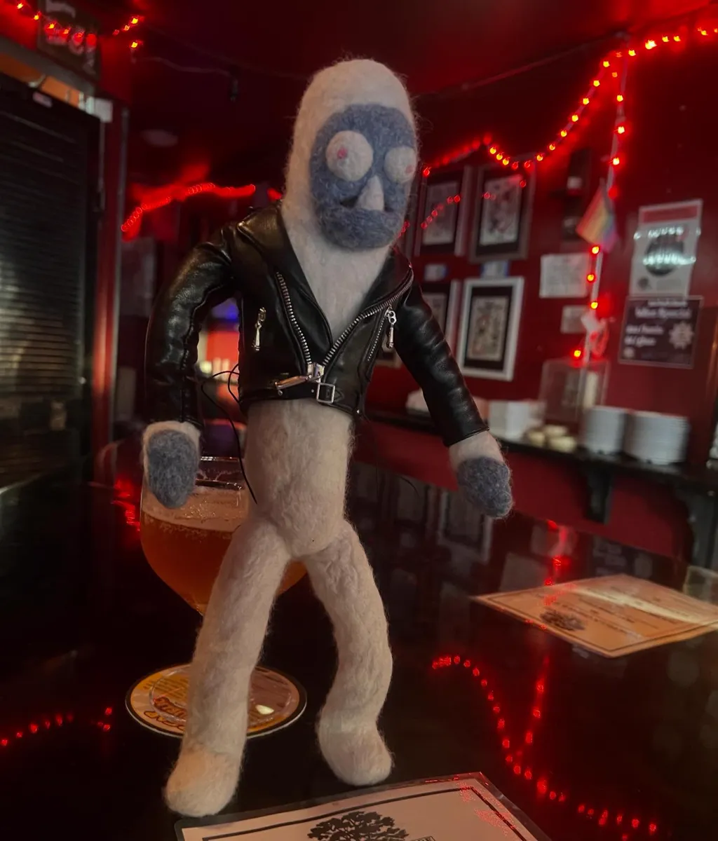 Freddi Yeti wearing a tiny black leather jacket, standing on a bar in red light