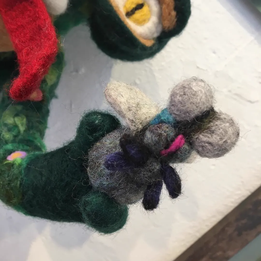 Close-up of a small felted fly held in a green felted hand