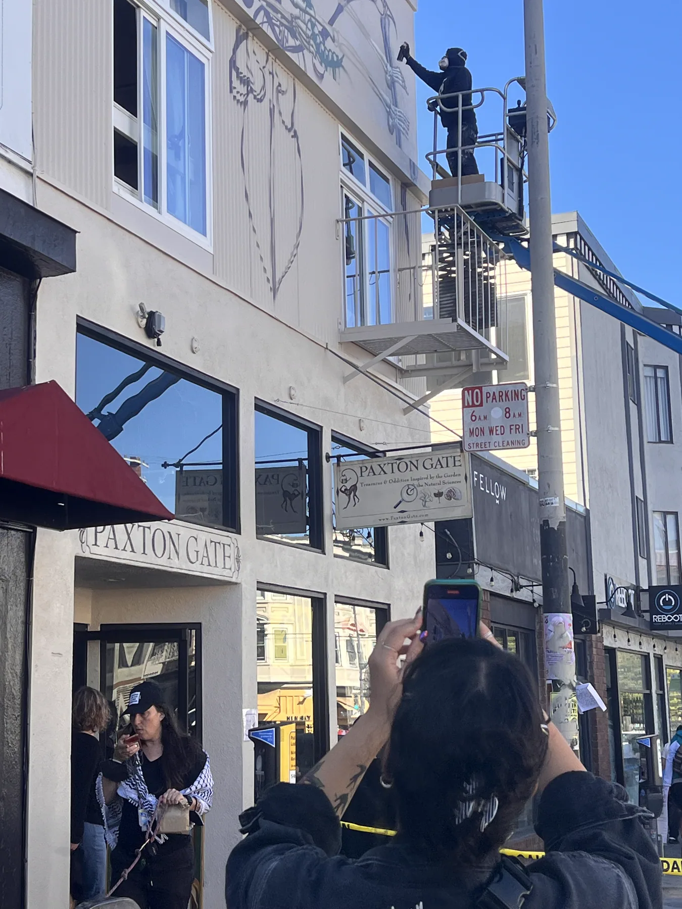 People on the sidewalk stopping to watch the mural being painted